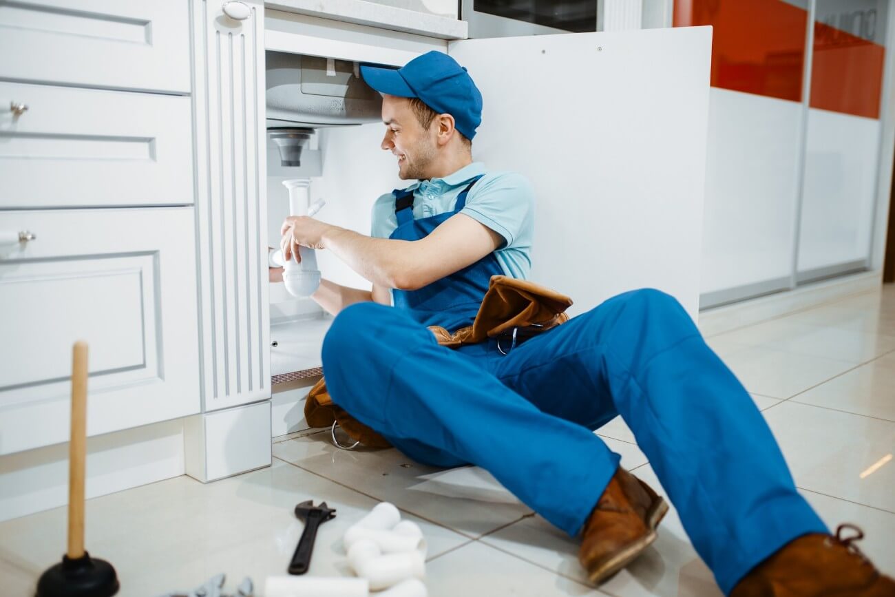 plumber in uniform holds drain pipe in the kitchen