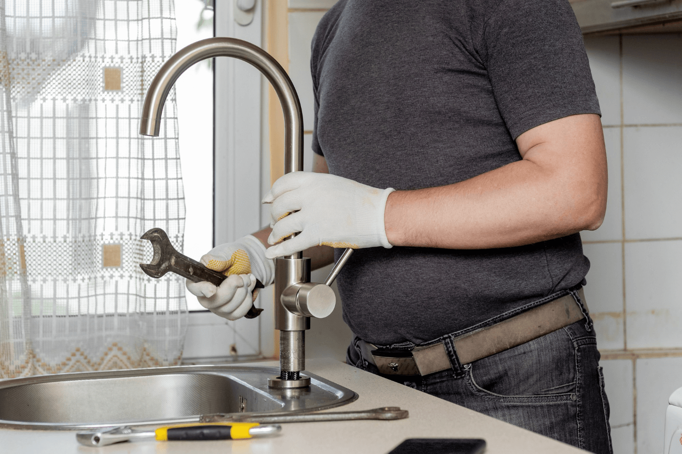 A plumber in the kitchen installs a new water tap.